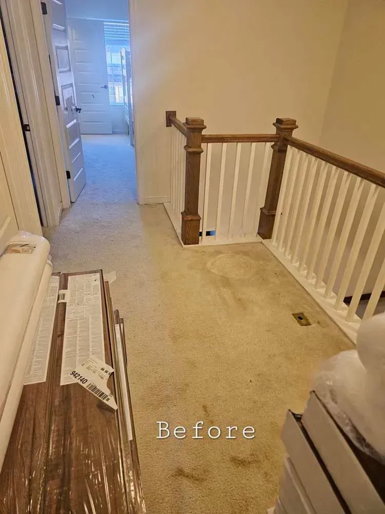 Hallway with beige carpet, stairs with wooden railing, and doors leading to other rooms.