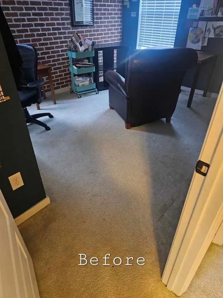 A room with beige carpet and dark furniture. A brick wall is in the background. The word 