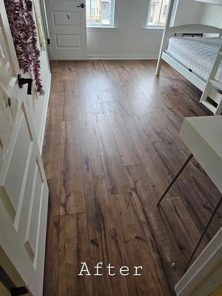 Wood flooring installed in a bedroom, seen from doorway. White bunk bed, desk, and door frames against white walls.