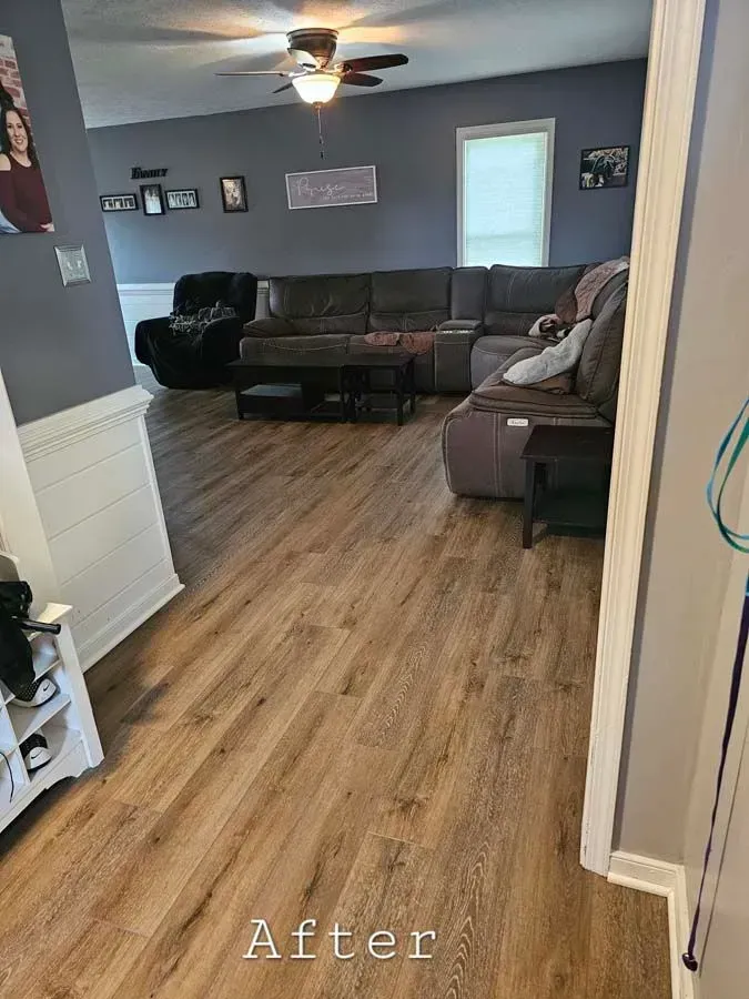 A living room with brown flooring, gray walls, a sectional sofa, and a ceiling fan.