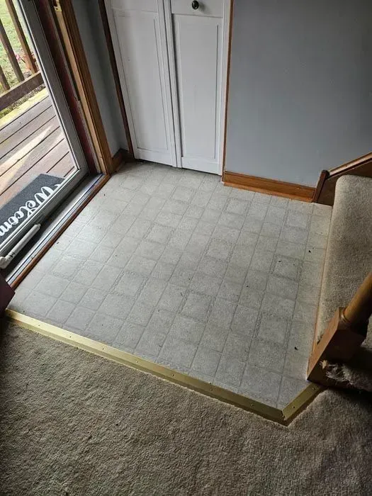 Entryway with tiled floor, carpet, door, and stairs. Gold threshold.