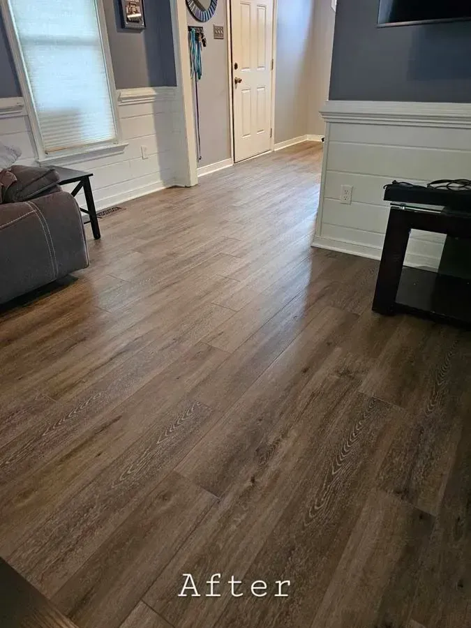 Newly installed wood-look laminate flooring in a living space with white wainscoting and gray walls.