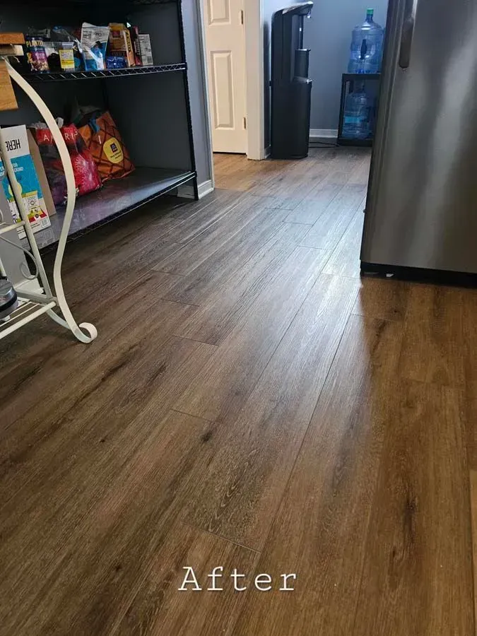 Dark wood-look flooring in a kitchen area with a partially visible pantry and refrigerator.
