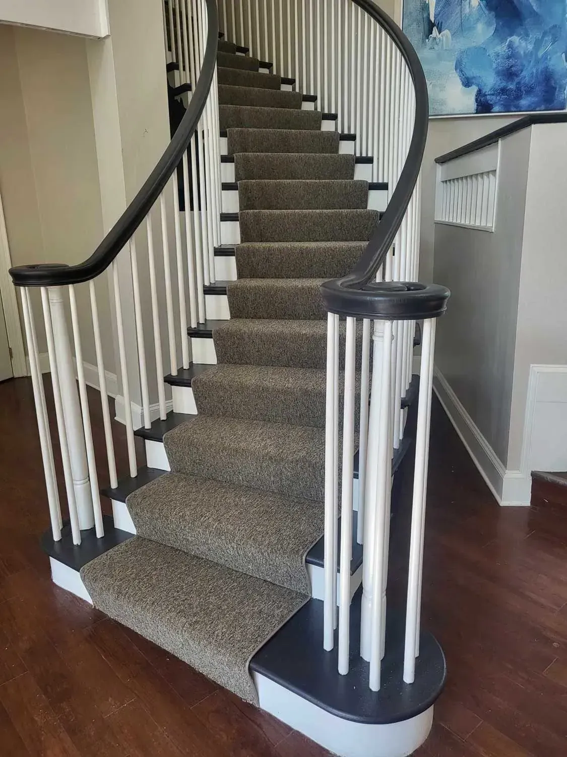 Curved staircase with carpeted steps, white balusters, and dark handrail.