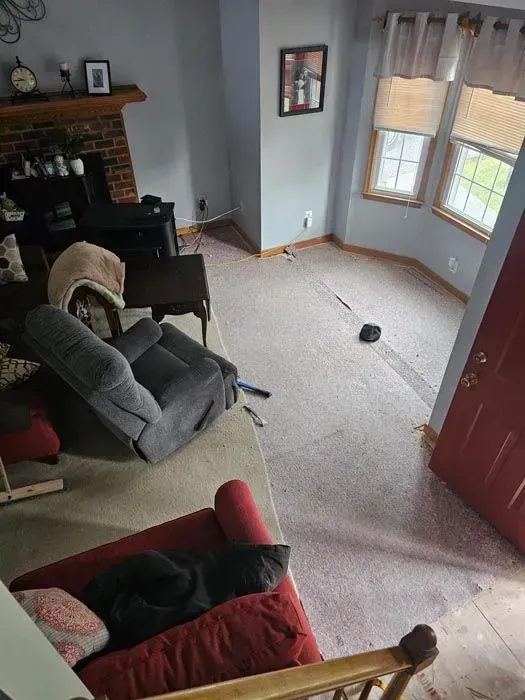 Living room scene with damaged carpet, recliner, couch, fireplace, and open doorway.