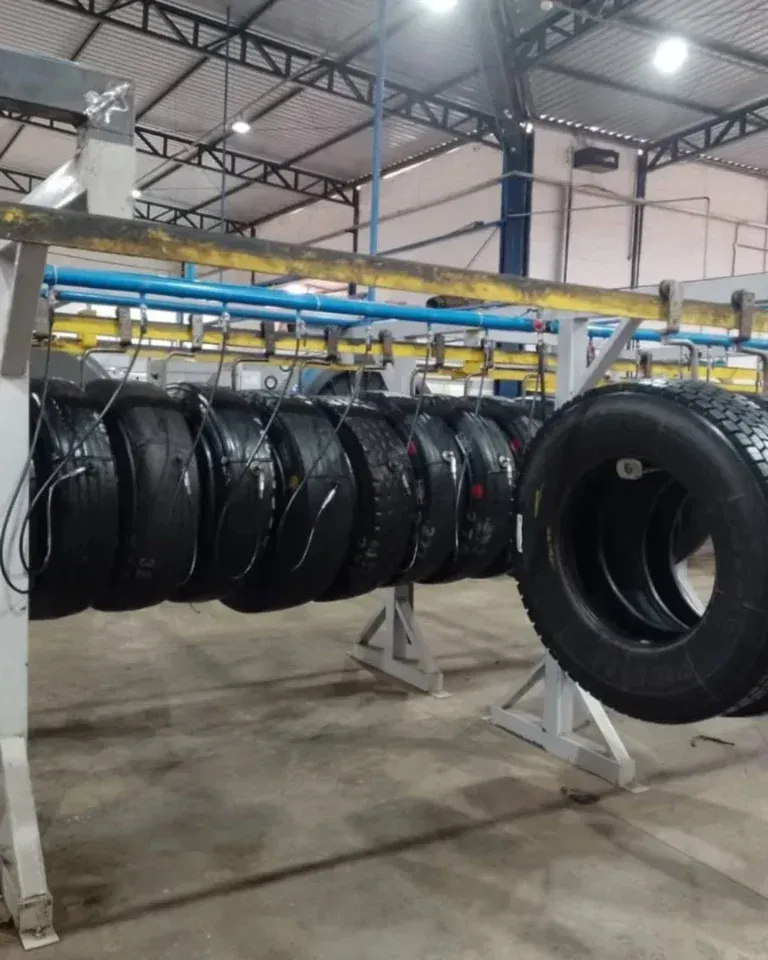 Pneus pendurados em um suporte em uma fábrica, provavelmente para inspeção ou processamento.