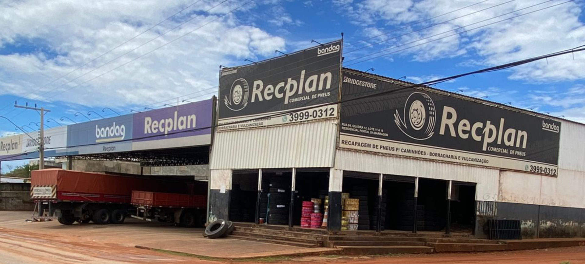 Oficina mecânica com carros em elevadores e mecânicos trabalhando. A marca Bridgestone está visível.