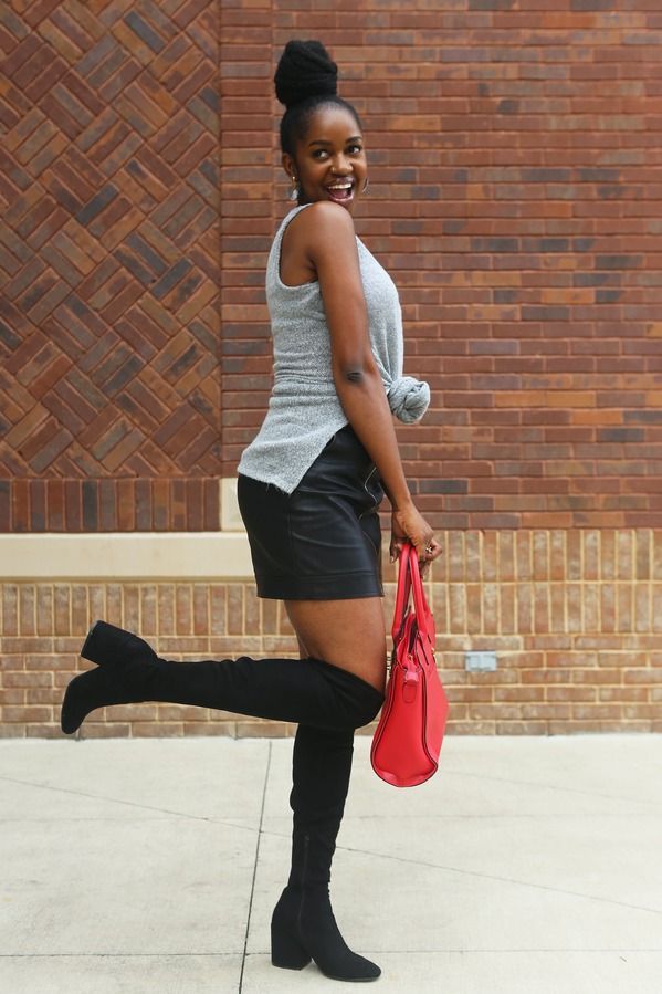 A woman wearing over the knee boots is holding a red purse.