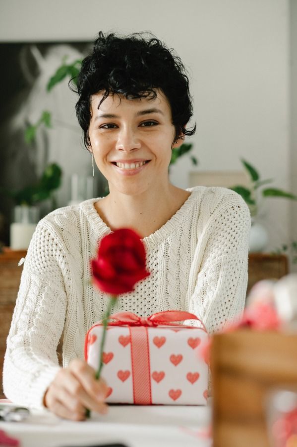 A woman is holding a red rose and a gift box.