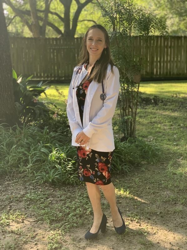 Erica wearing a lab coat and a stethoscope is standing in a yard.