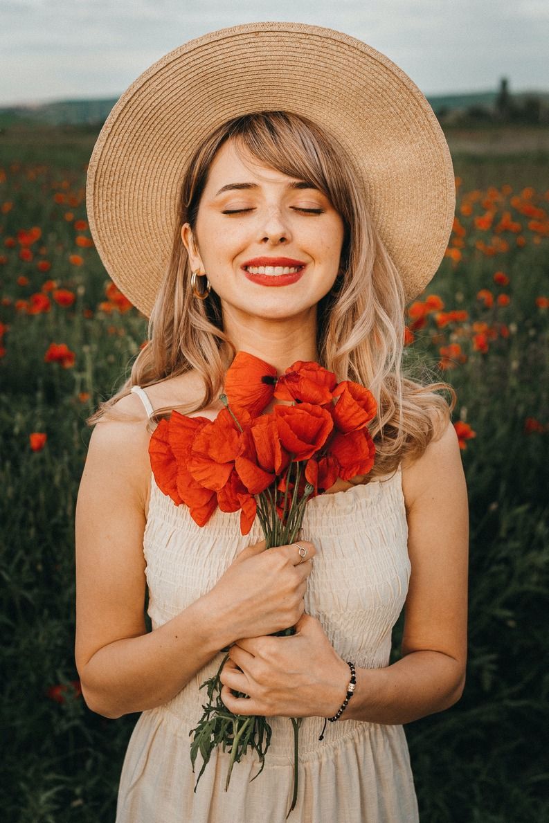 A woman in a straw hat is holding a bouquet of red flowers in a field.