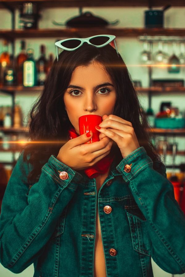 A woman in a denim jacket is drinking from a red cup.