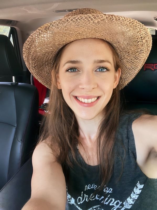 Erica wearing a straw hat is taking a selfie in a car.