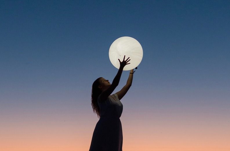 A woman is holding a full moon in her hands.