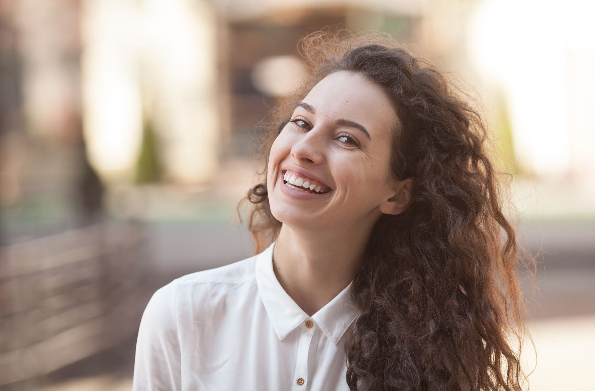 A woman with curly hair is smiling and looking up.