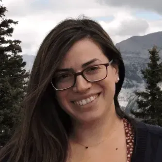 A woman wearing glasses and a necklace is smiling for the camera.