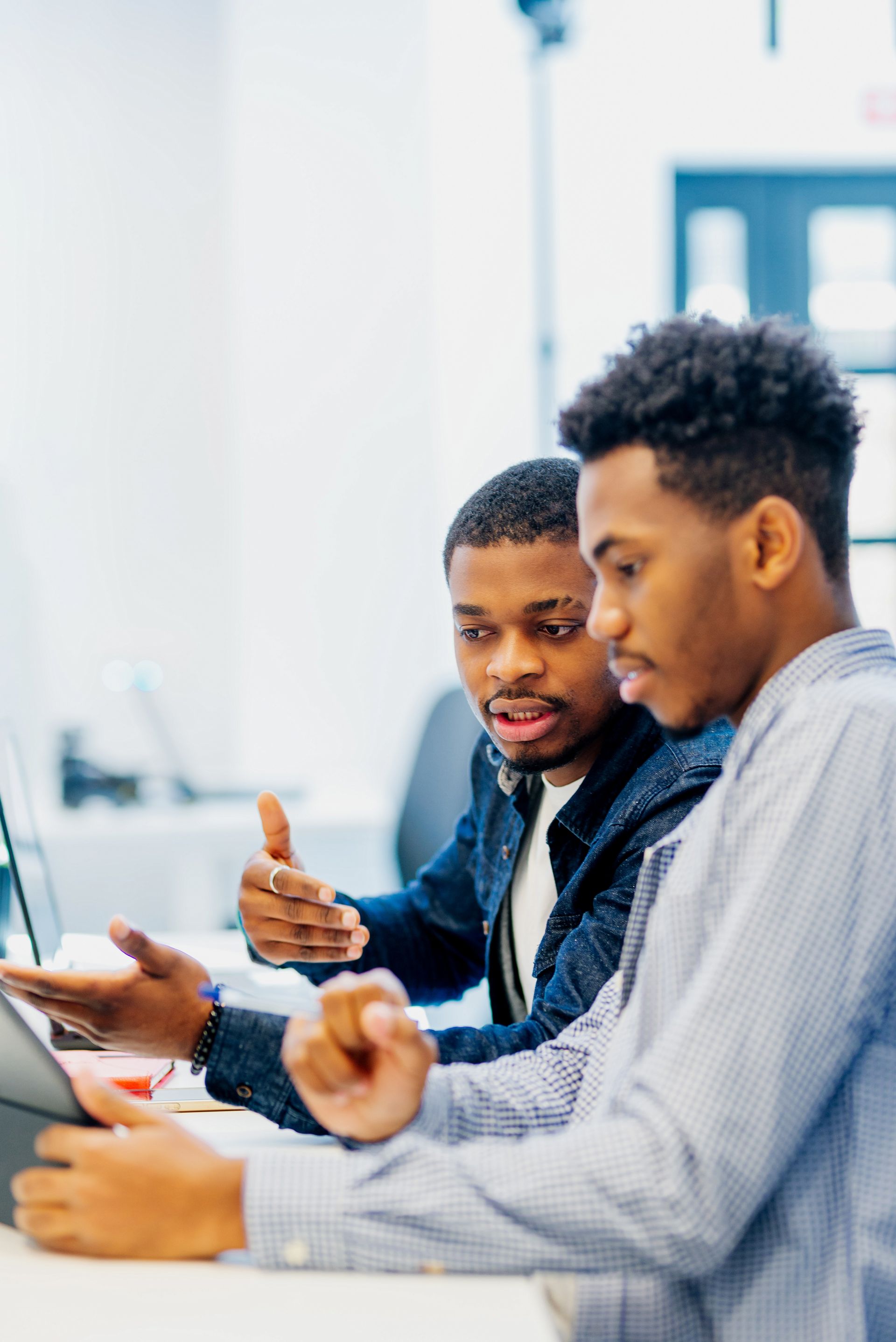 Two young men are sitting at a desk looking at a computer screen.