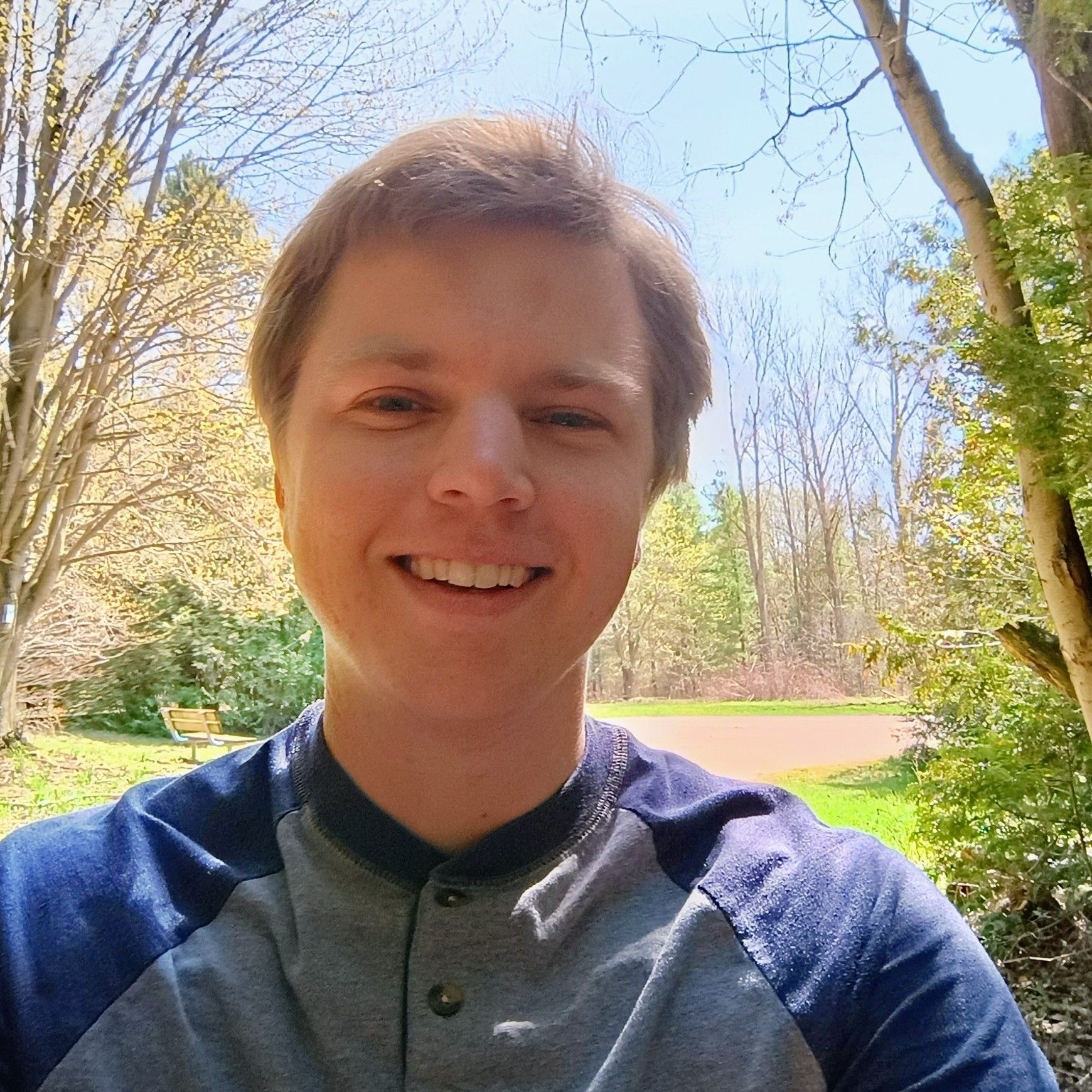 A man wearing a blue and grey shirt is smiling for the camera.