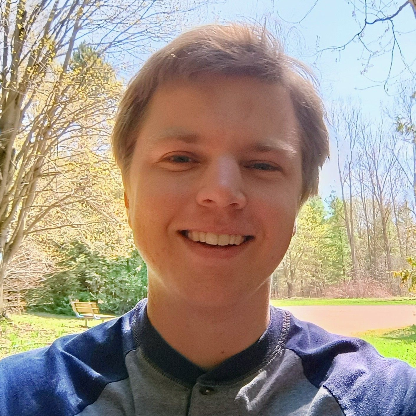 A man wearing a blue and grey shirt is smiling for the camera.