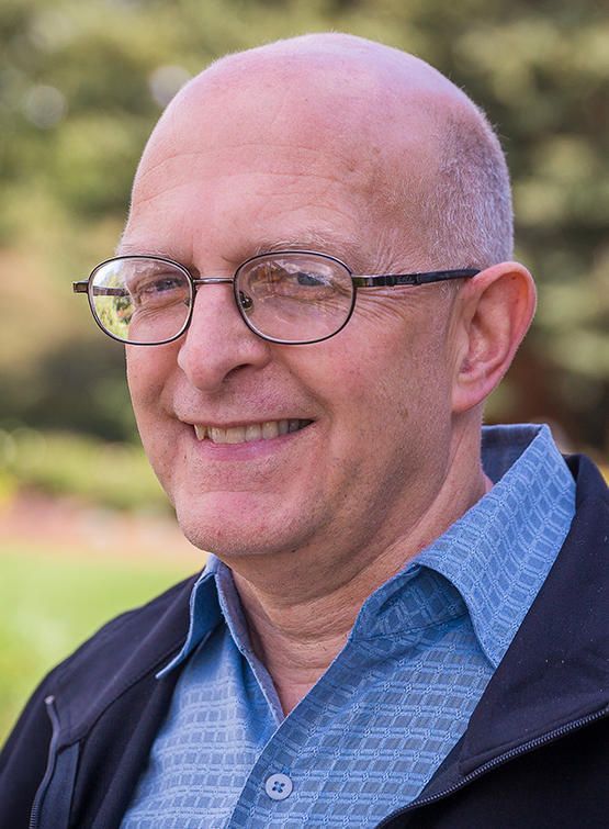 A man wearing glasses and a blue shirt is smiling