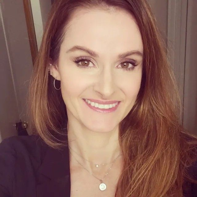 A woman wearing a necklace and earrings is smiling for the camera.