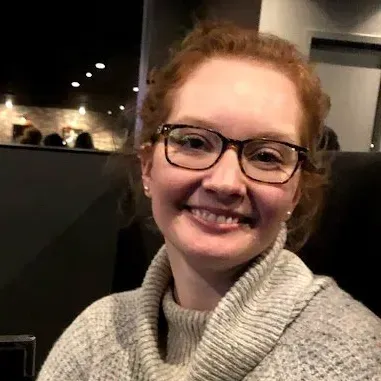 A woman wearing glasses and a sweater is smiling for the camera.