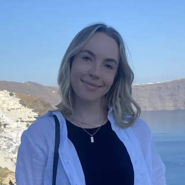 A woman wearing a black shirt and a white shirt is standing in front of a body of water.