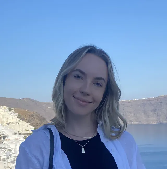 A woman wearing a black shirt and a white shirt is standing in front of a body of water.