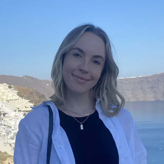A woman wearing a black shirt and a white shirt is standing in front of a body of water.