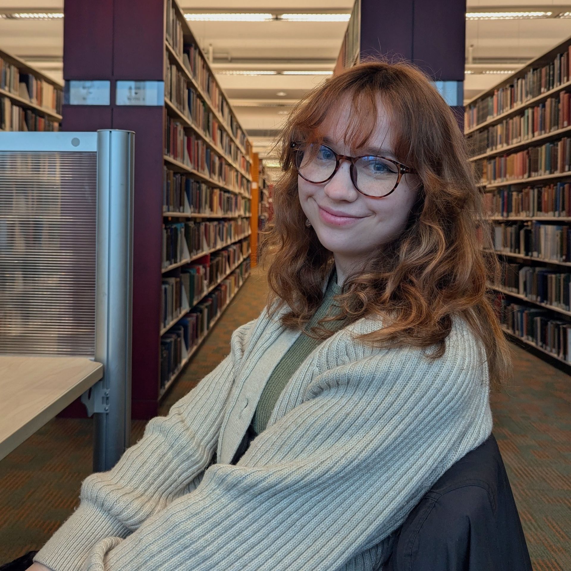 A woman wearing a white sweater and eyeglasses is smiling for the camera.
