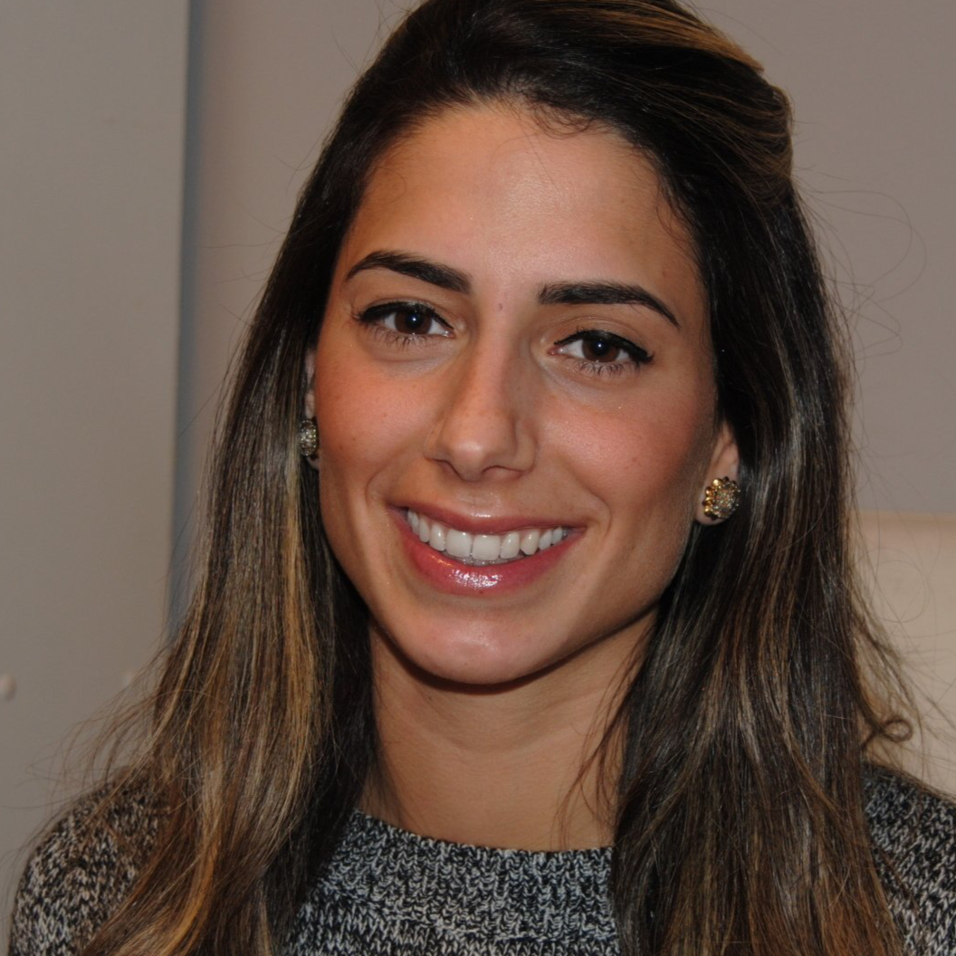 A woman wearing a grey sweater and earrings smiles for the camera.