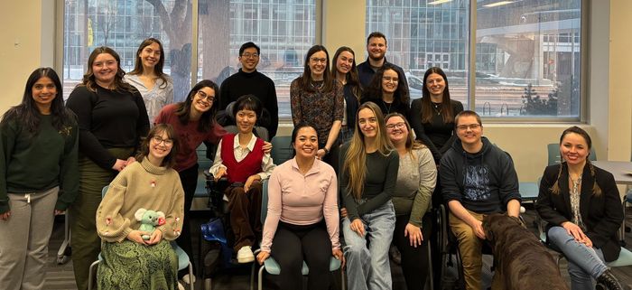 Group of people posing together indoors in front of large windows, smiling in a casual office setting.