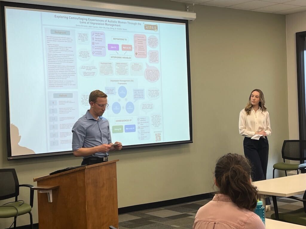 A man and a woman are giving a presentation in front of a large screen in a classroom.