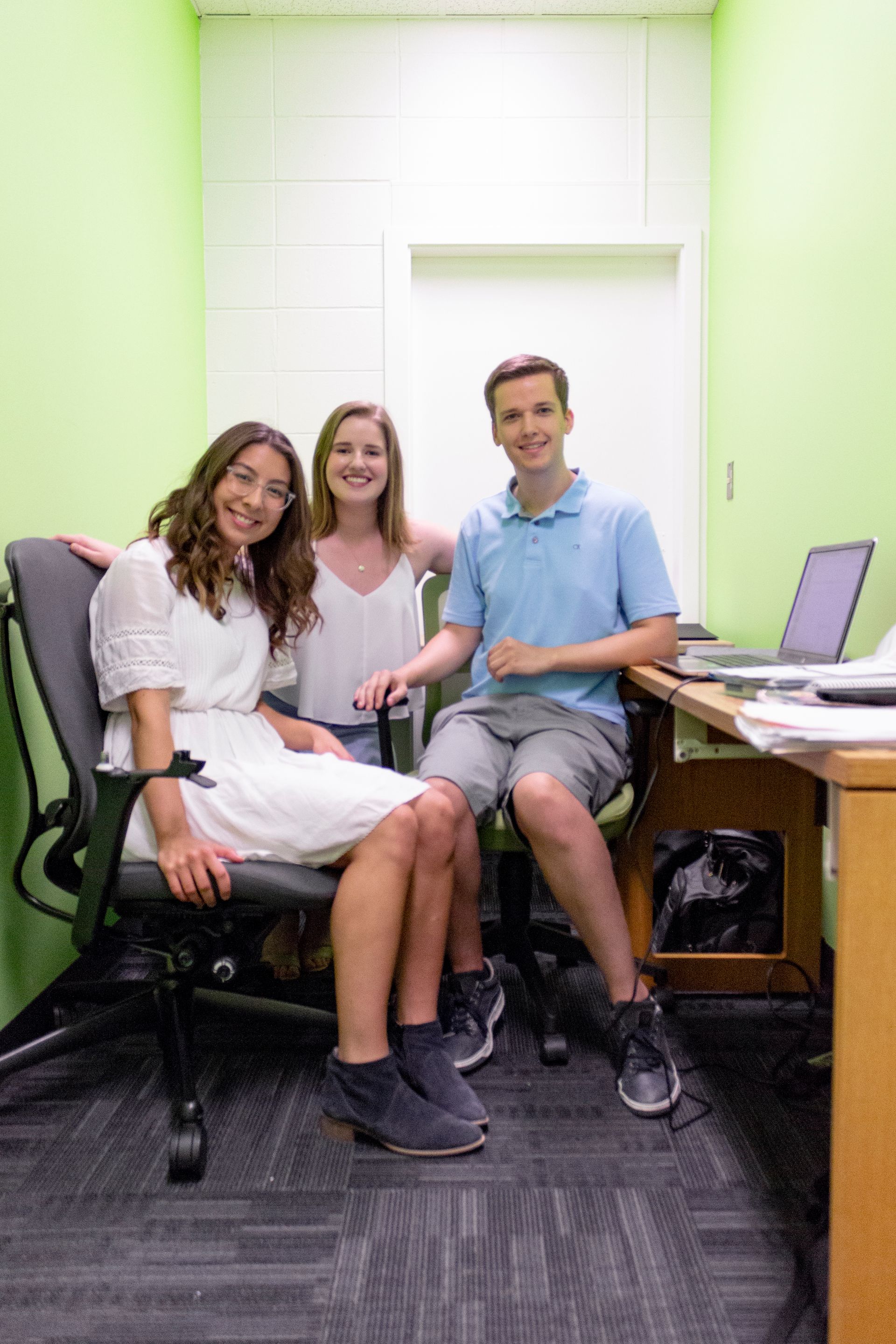 A man and two women are sitting in chairs in an office.