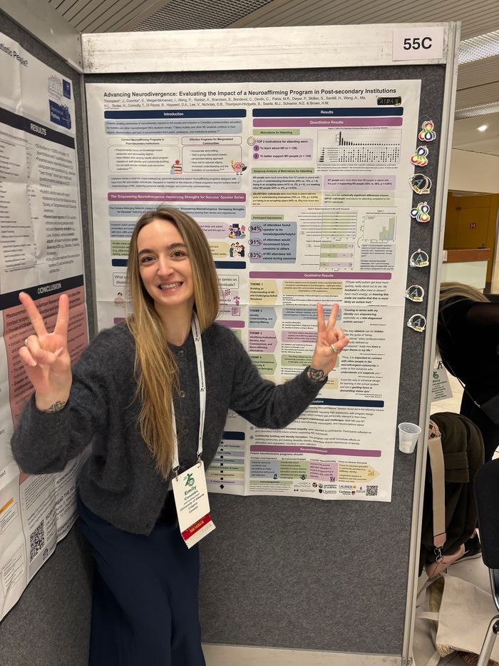 Woman posing with peace signs beside a colorful academic poster at a conference.