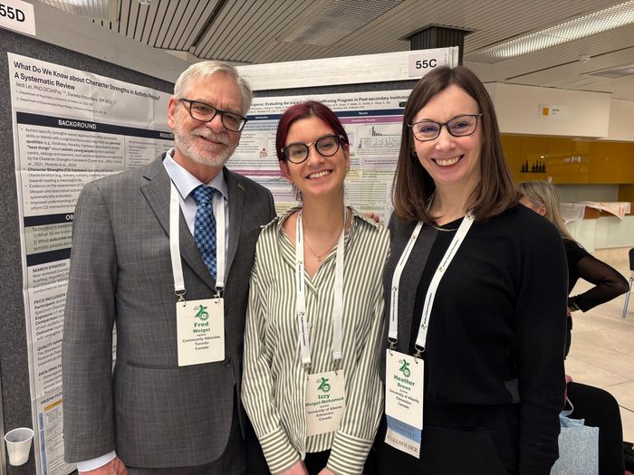 Three people smiling at a conference poster session, standing in front of a presentation board.