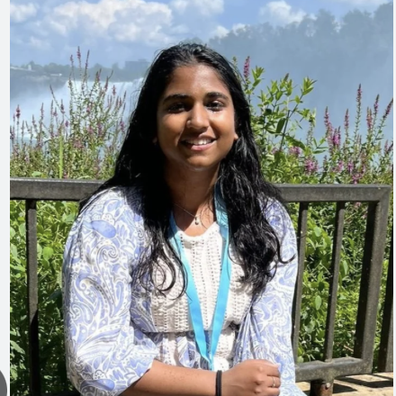 A woman in a paisley shirt wearing a blue lanyard is smiling for the camera.