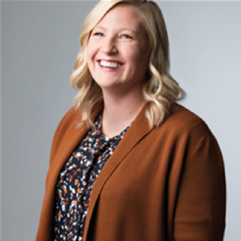 A woman wearing a brown cardigan and a floral shirt is smiling