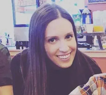 A woman is smiling while sitting at a table in a restaurant.