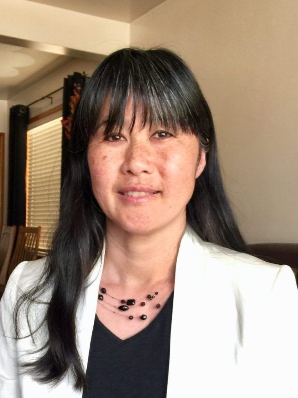 A woman with a black shirt and white blazer is smiling