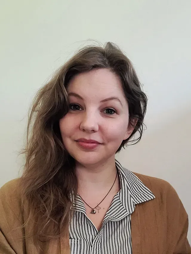 A woman wearing a striped shirt and a brown cardigan is smiling for the camera.