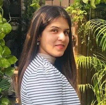 A woman in a striped shirt is standing in front of a bush.