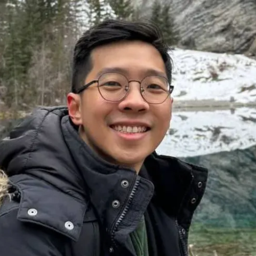 A man wearing a winter jacket and eyeglasses is smiling for the camera.