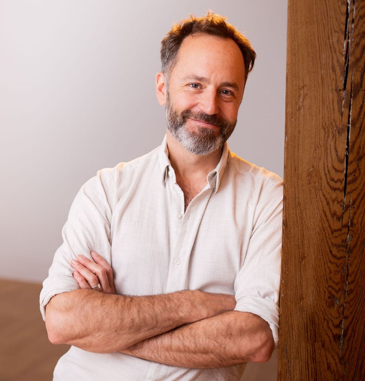 A man with a beard is leaning against a wall with his arms crossed