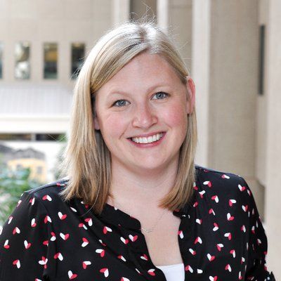 A woman wearing a brown cardigan and a floral shirt is smiling