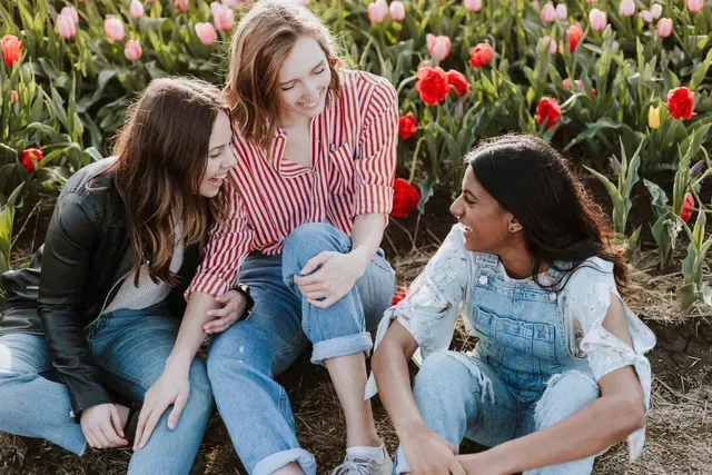 Three women are sitting on the ground in a field of flowers.