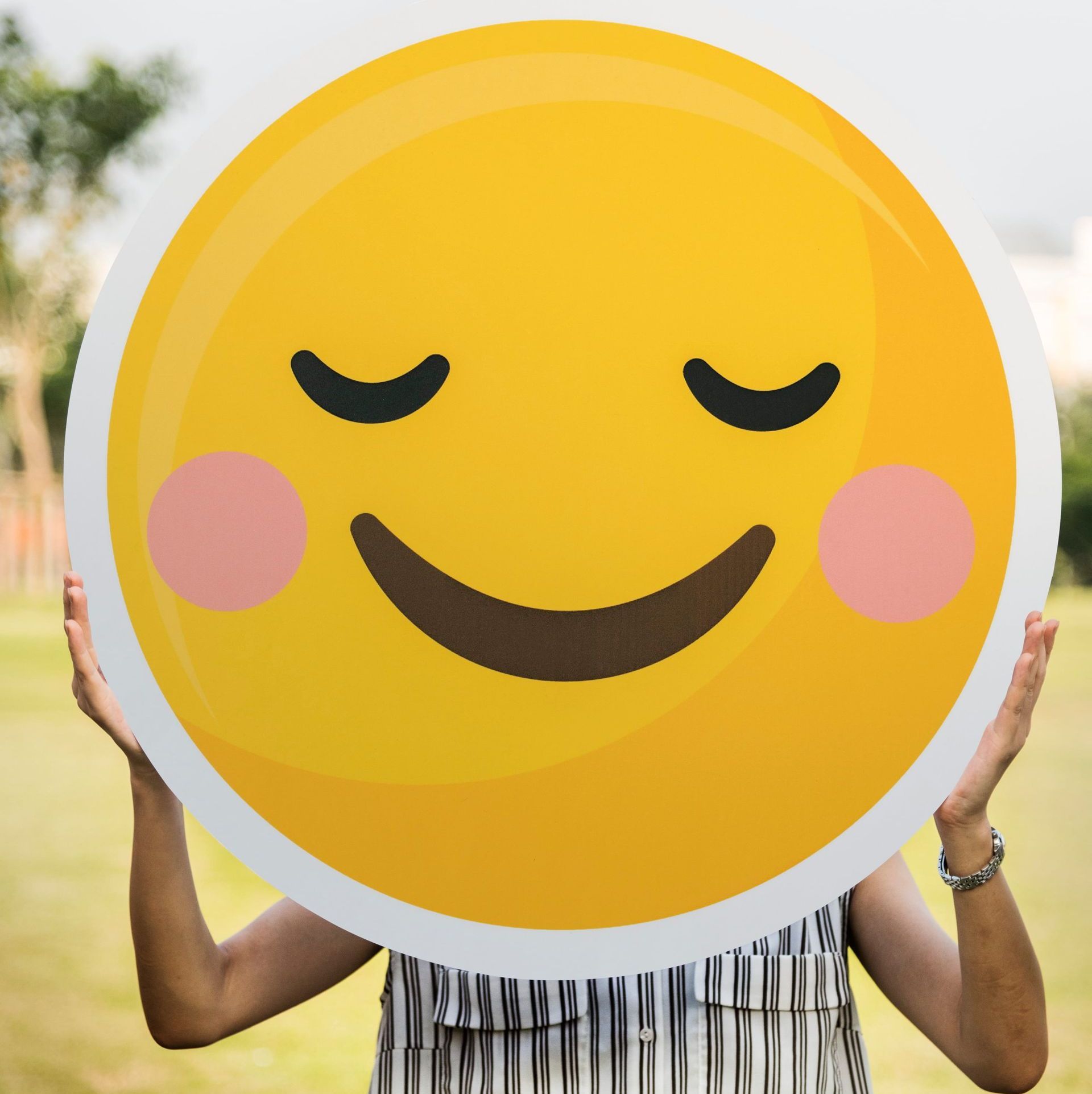 A woman is holding up a smiley face with her eyes closed