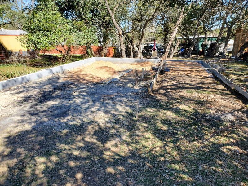 A concrete driveway is being built in a yard with trees in the background.