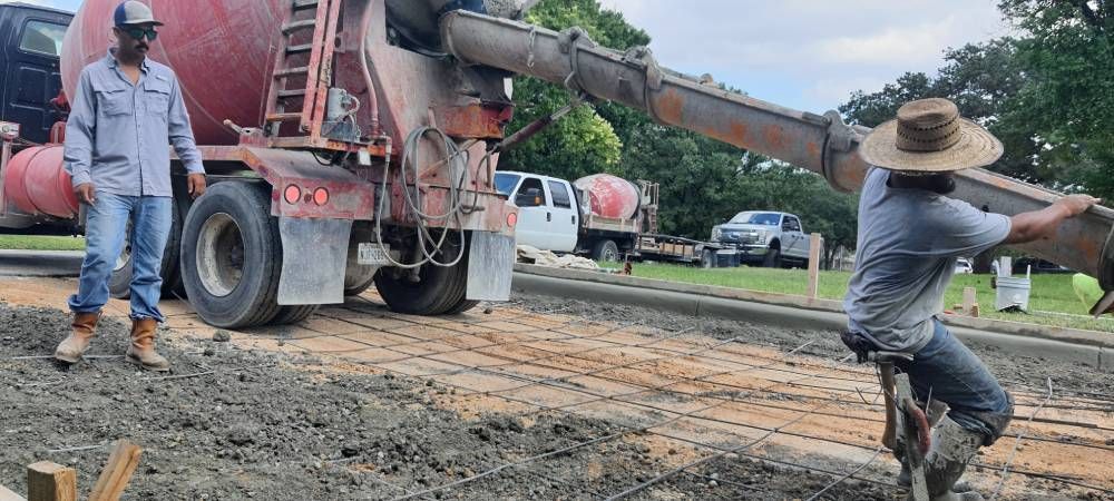 A man is kneeling in the dirt next to a concrete truck.