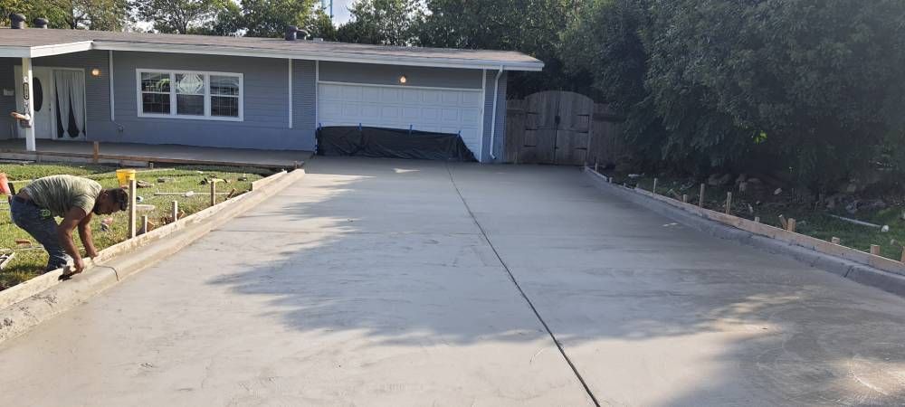 A man is working on a concrete driveway in front of a house.